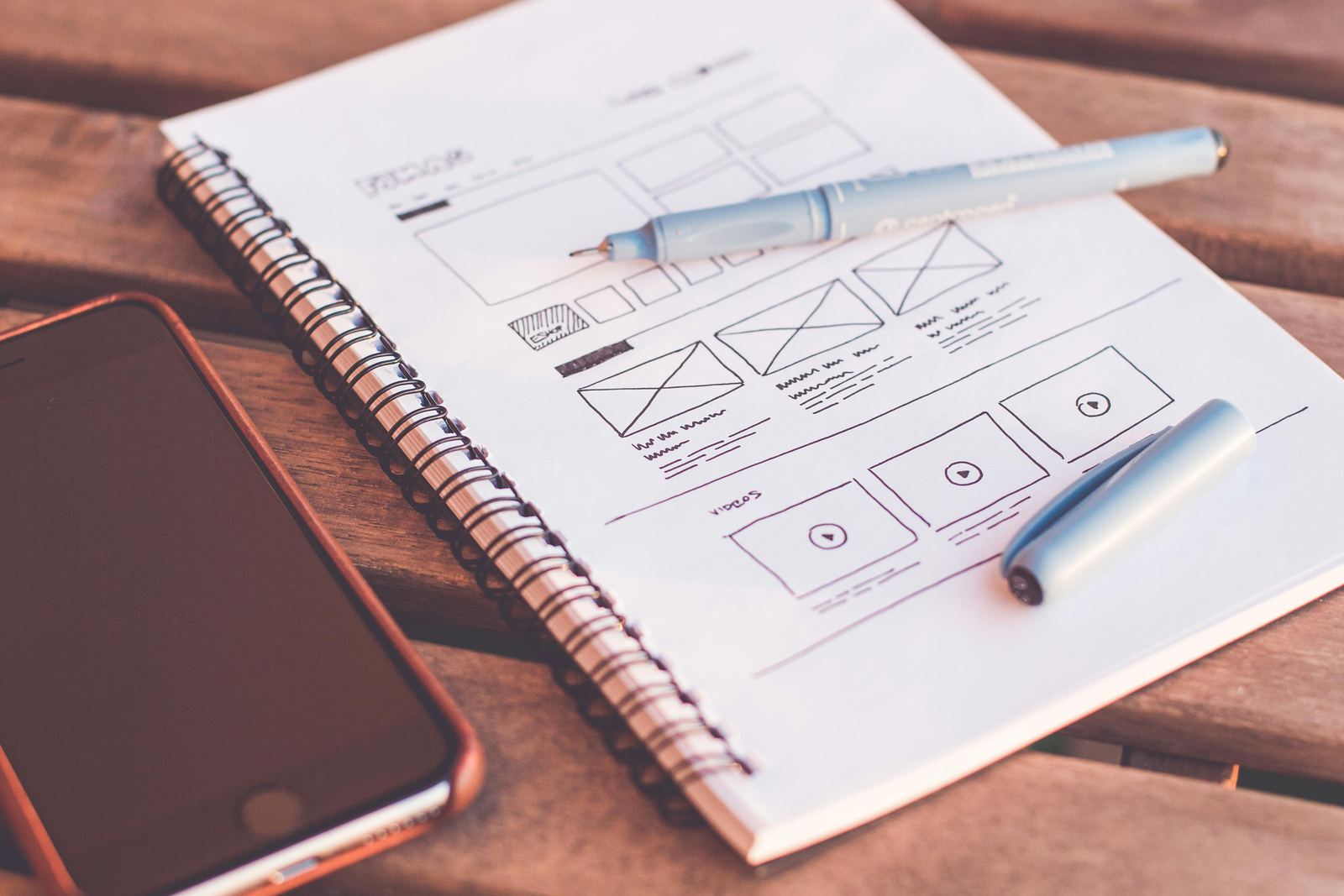 Hand-drawn website wireframes on a notebook beside a smartphone